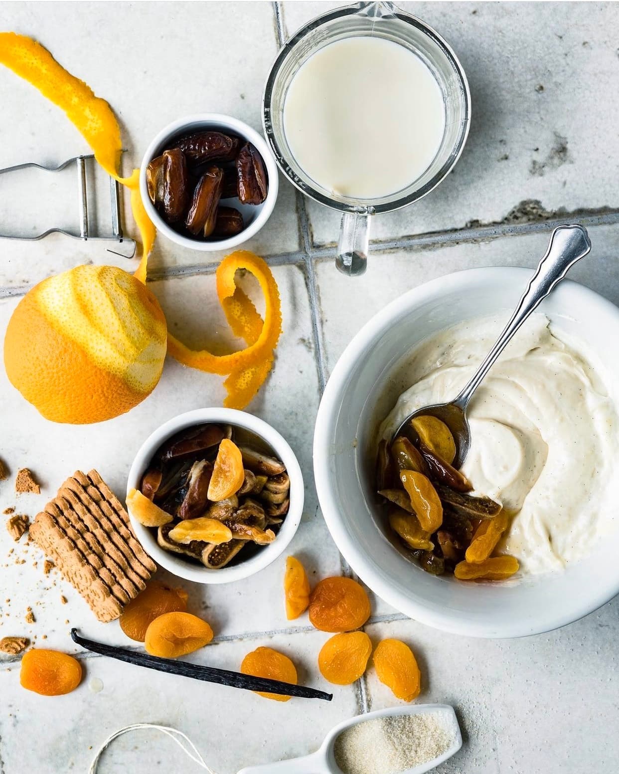Coco Anjela ingredients laid out overhead — dates, apricots, figs, vanilla, orange, oat milk, vegan cream